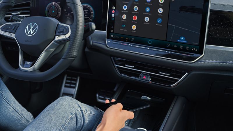 Detailed view of the cockpit in the VW Passat. Someone is sitting in the driver seat and holding a smartphone in their hand.