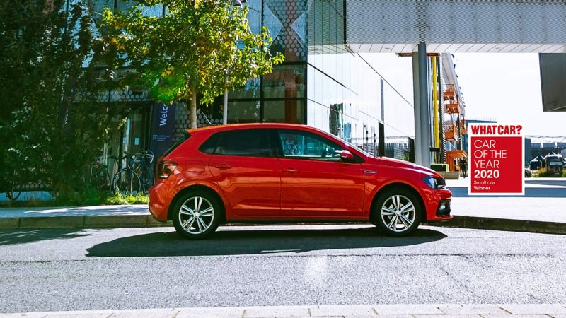 A red Volkswagen Polo parked outside an office building.