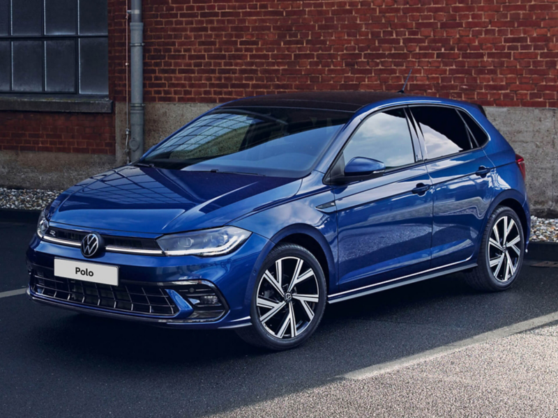 A blue Polo R-Line is parked on pavement in front of brick wall