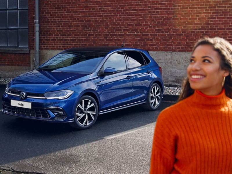 A blue Polo parked in a car park with a woman walking away from it smiling
