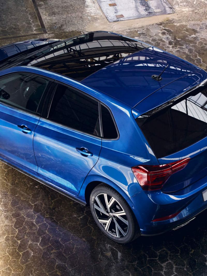 A blue VW Polo with a panoramic sliding roof is parked in a hall