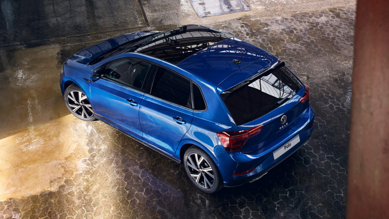 A blue VW Polo with a panoramic sliding roof is parked in a hall