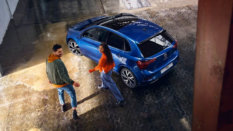 View from above of a dark blue polo with a couple walking towards it smiling.