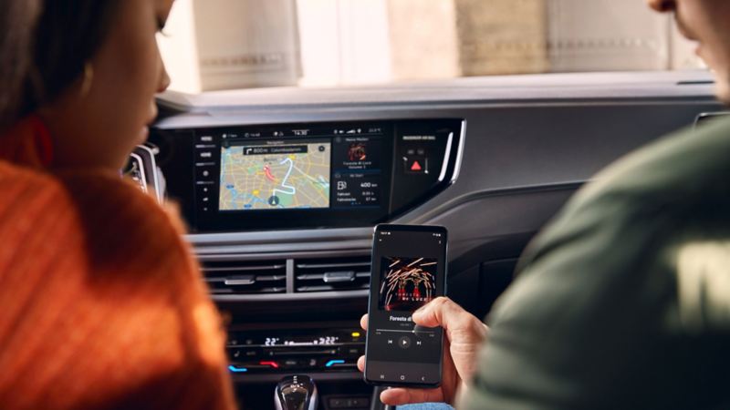 Two people are sitting in the front of the VW Polo, a smartphone is held up from the right and connects wirelessly to the infotainment system.