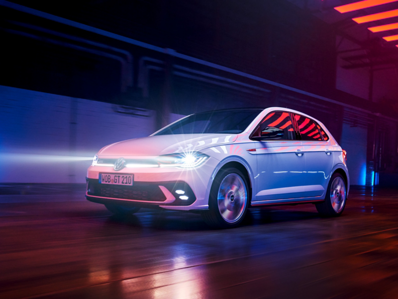 A white VW Polo GTI is driving in a hall with the LED matrix headlights and light bar in the front switched on.