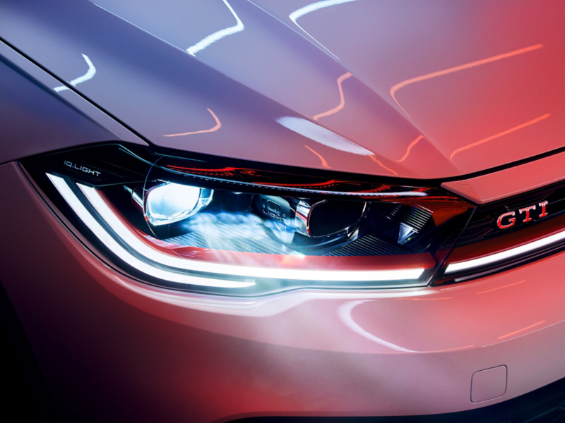 Close-up of the LED matrix headlights in the front of a VW Polo GTI in white, red trim strip and GTI badge visible.