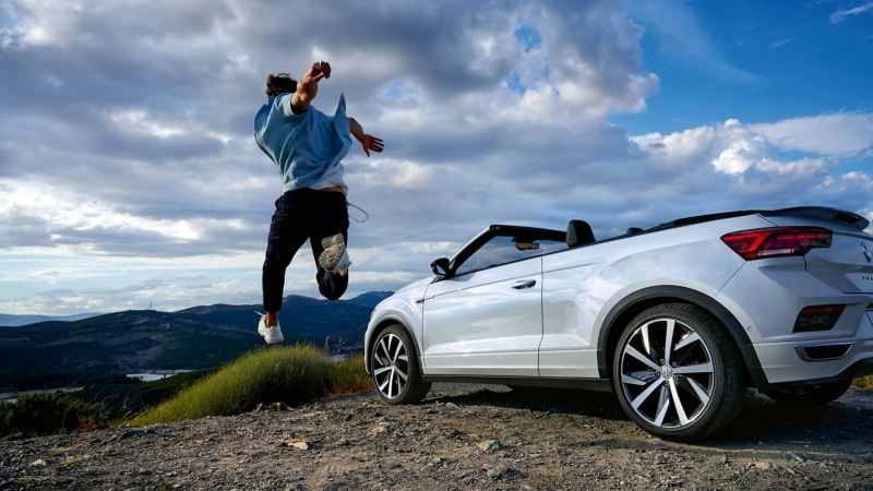 A white Volkswagen T-Roc Cabriolet parked with a man jumping next to it