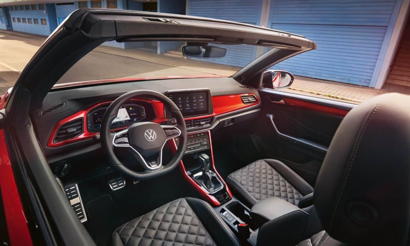 Interior of the VW T-Roc Cabriolet: View through the open roof from above onto the cockpit with red decoration and the front seats.