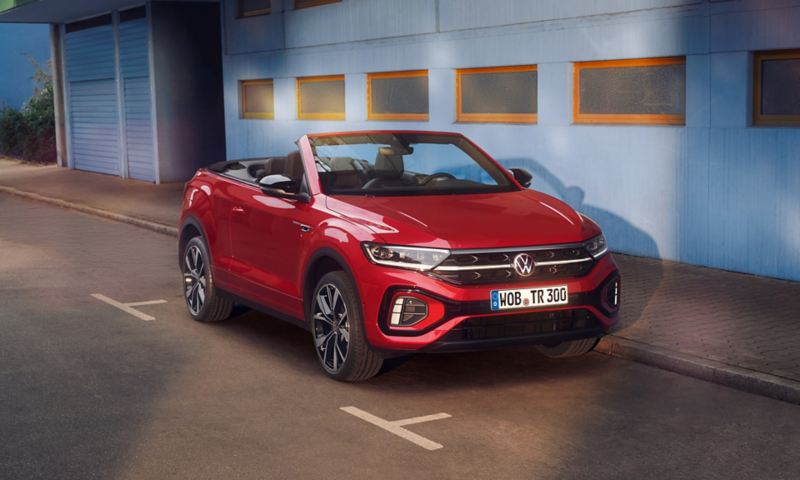 Front and side view of the red T-Roc Cabriolet with the roof open, parked on the side of the road.