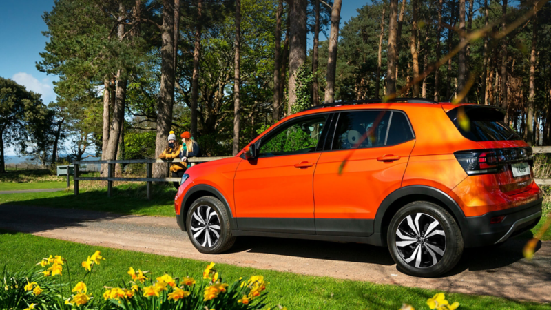 An orange VW T-Cross on a park road