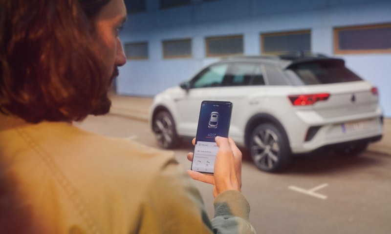VW T-Roc R-Line in white in front of a building, side visible, man with smartphone in foreground