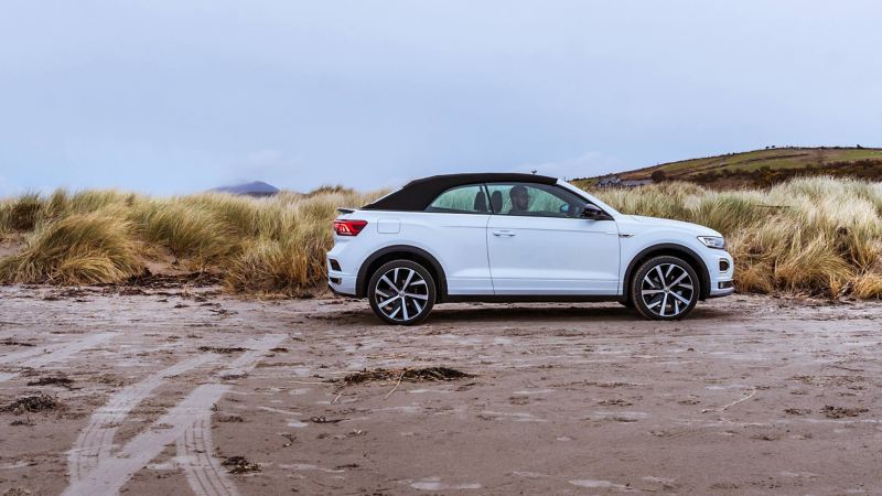 A man sitting in a white T-Roc Cabriolet on the beach