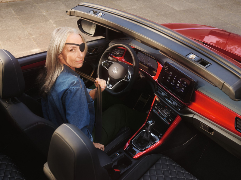 Person with eyepatch sits inside red VW T-Roc cabriolet looking up whilst roof is down