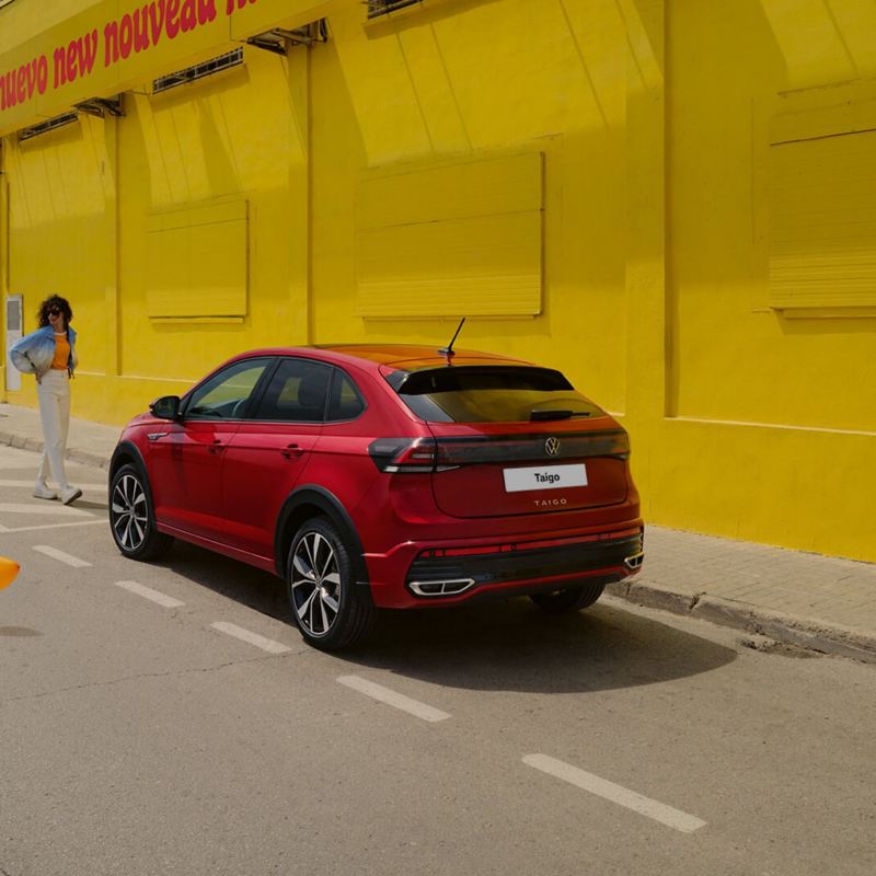 A person stands in front of a red Taigo on a street next to a yellow wall