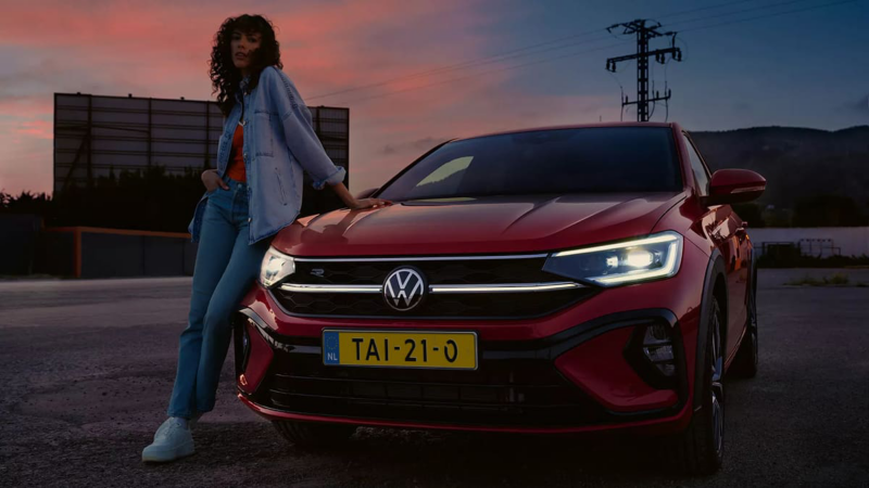 Vooraanzicht rode Volkswagen Taigo, focus op matrix koplampverlichting, vrouw leunt tegen de Taigo