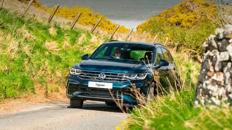 A blue VW Tiguan driving up a windy road in sunny countryside