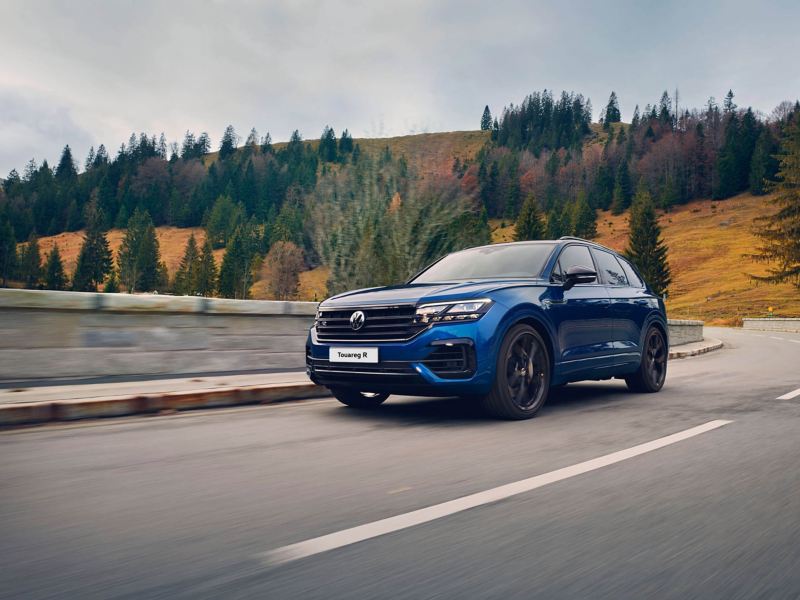 A blue Volkswagen Touareg R drives along a mountain road