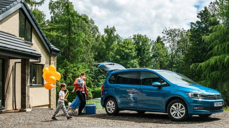 A VW Touran parked in front of a house with a family loading the boot for a day out