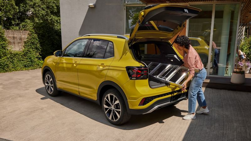 A lady putting a ladder into the boot of a yellow T-Cross