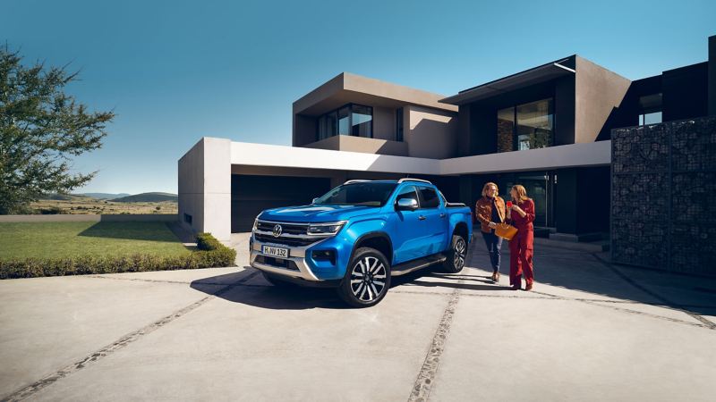 Blue Amarok parked in front of a modern house with a couple walking next to it. 