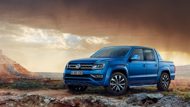 a blue Amarok on top of a mountain with a moody orange sky in the background