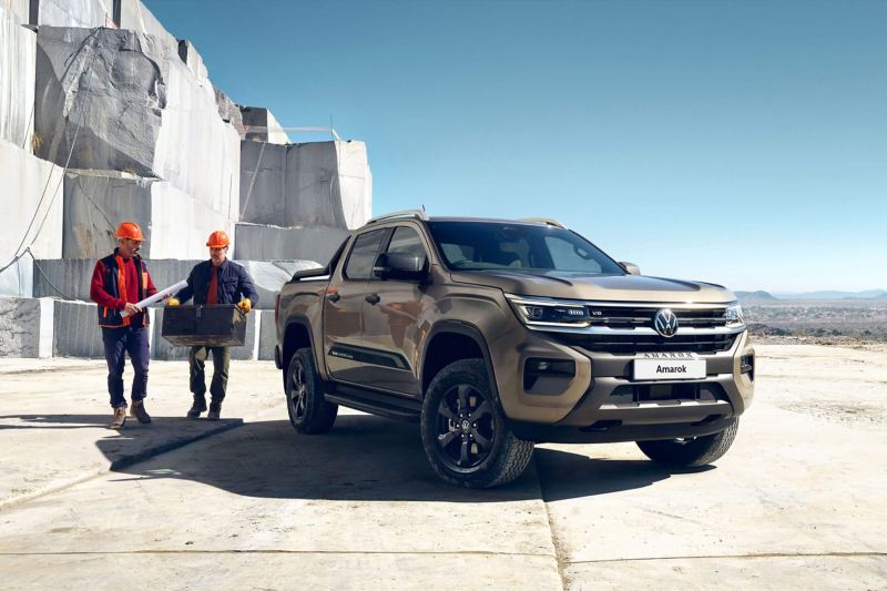Two workers standing next to a parked VW Amarok. 