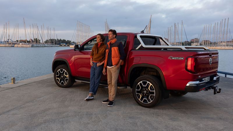 Photo of a red VW Amarok parked at a harbour side with a couple leaning against it.