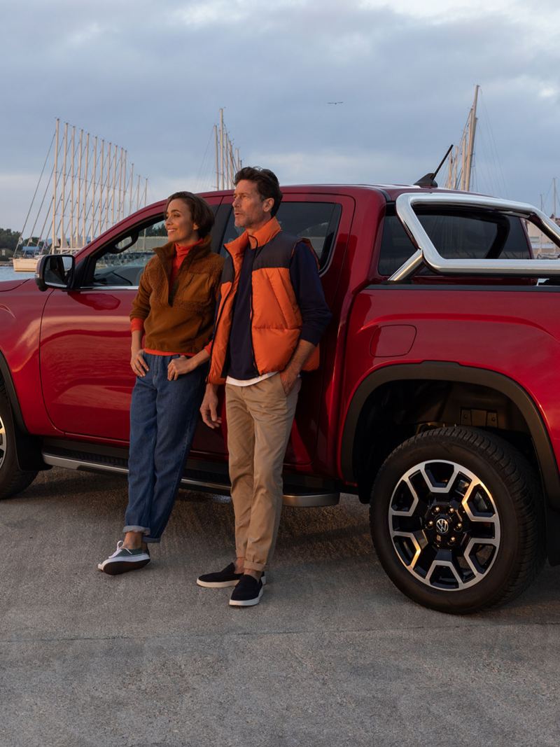 Photo of a red VW Amarok parked at a harbour side with a couple leaning against it.