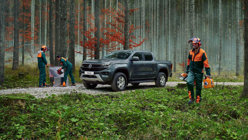 An Amarok parked in a forest, with workmen walking around it.