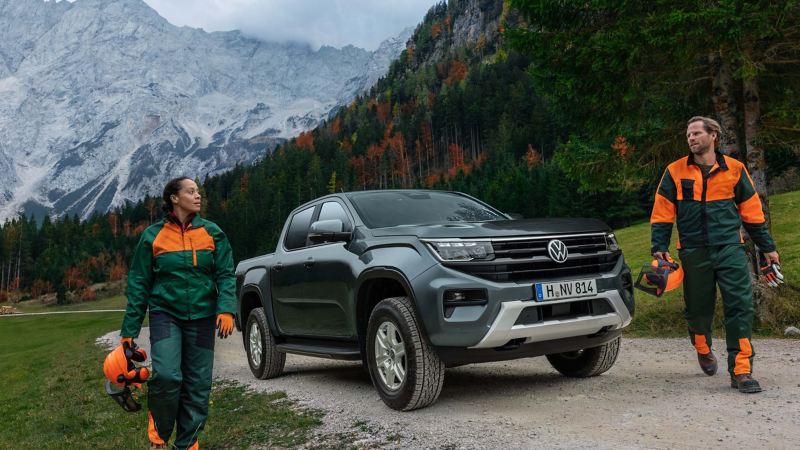 Photo showing 2 workers walking past an Amarok parked against a moutainous background.