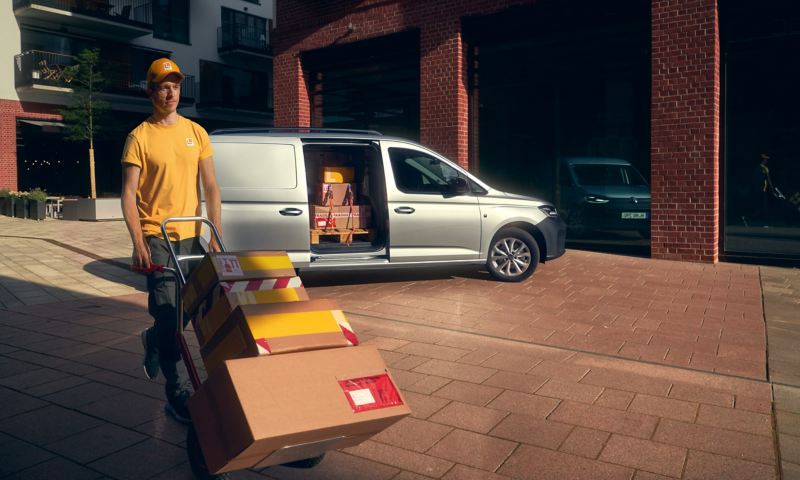 A delivery worker wheeling parcels away from a Caddy Cargo van