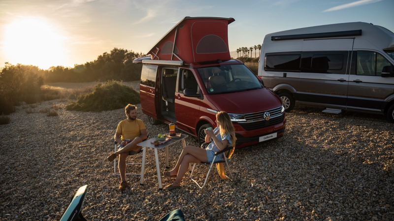 Photo of a couple setting up a camp next to their parked California. 