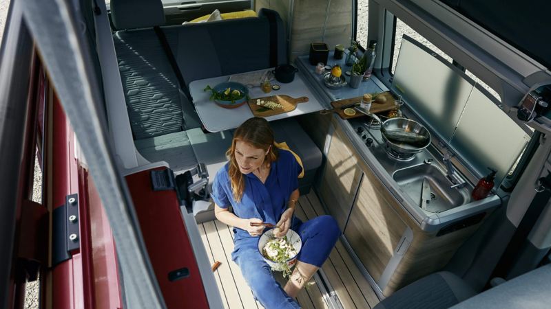 A photo showing the interior kitchen area of the California Surf with a woman sat on the vehicle floor eating food. 