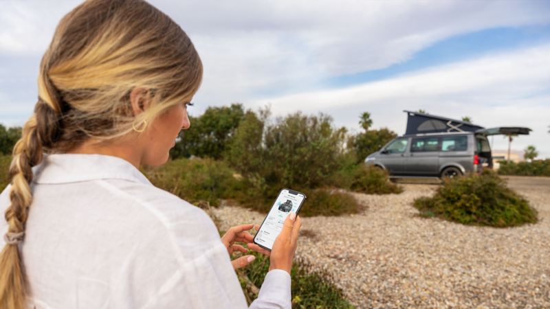 A person sits on a hill holding a smartphone with the California Remote Control.