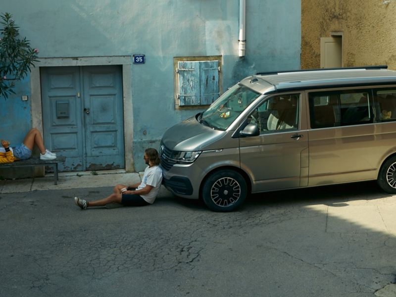 Two people sitting in the street with one of them leaning against a California Beach van