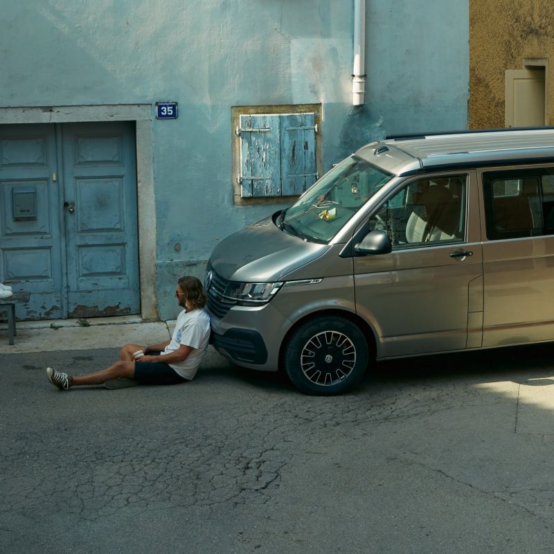 Two people sitting in the street with one of them leaning against a California Beach van