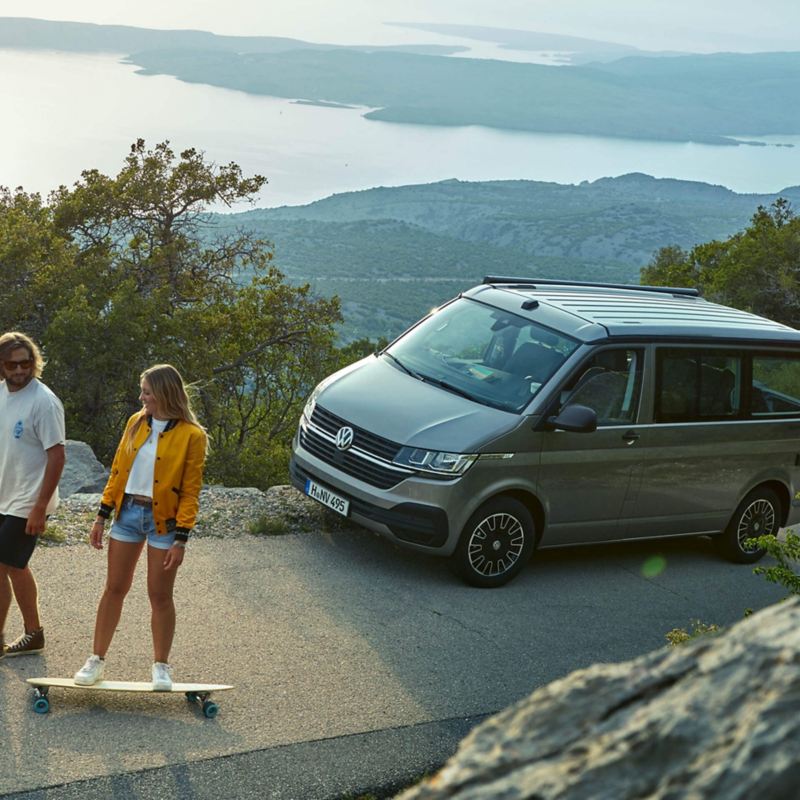 Two young people skateboarding passed a California Beach van