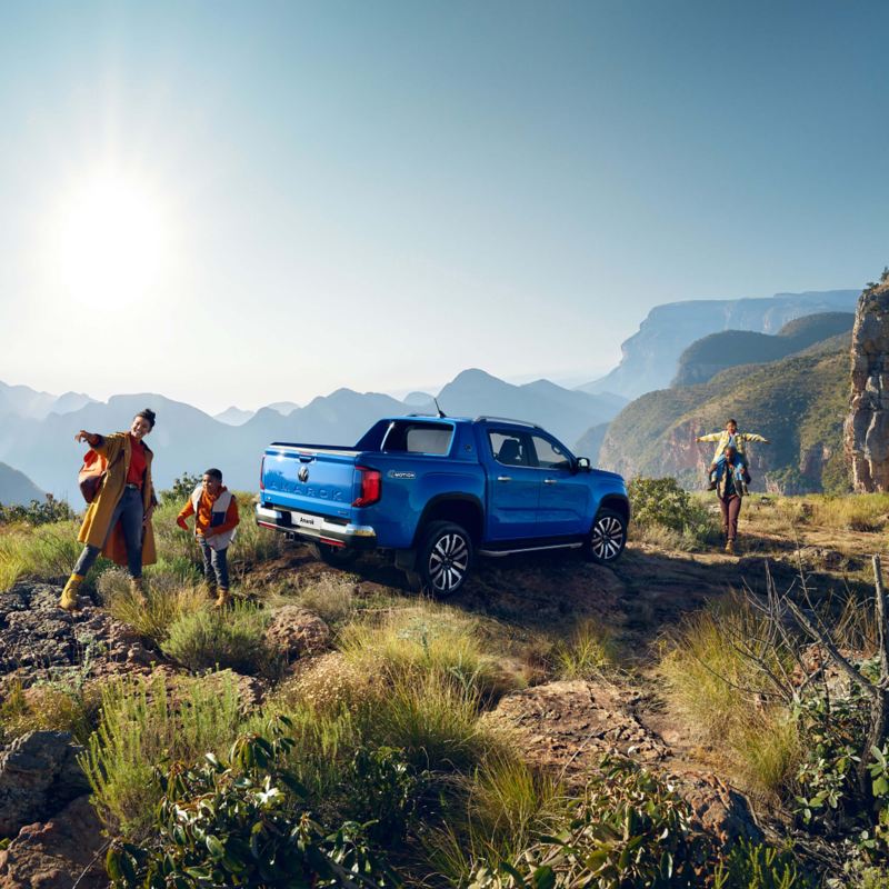 Photo of a family next to a parked blue VW Amarok against a mountainous background. 