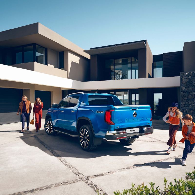 Photo showing a family around a blue Amarok parked outside of a modern house.