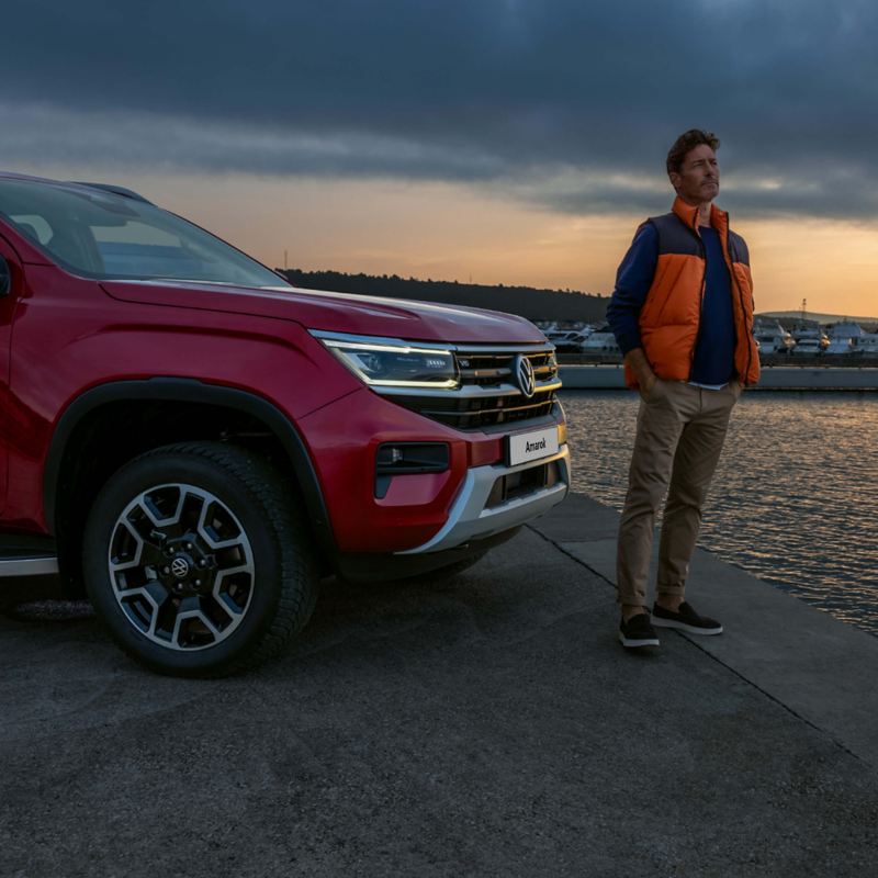 Photo of a man standing in front of a red VW Amarok parked at a harbour.