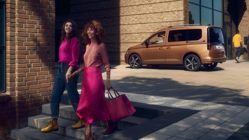 Two people walking away from a parked VW Caddy. 