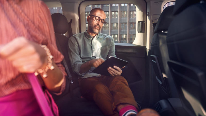 a man sitting back relaxing looking at a tablet in the Caddy