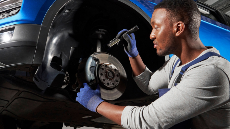A mechanic in gloves working on a vehicle's brake assembly underneath a car
