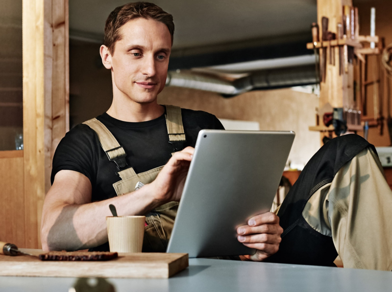 Person in workwear using a tablet at a workbench in a workshop setting.