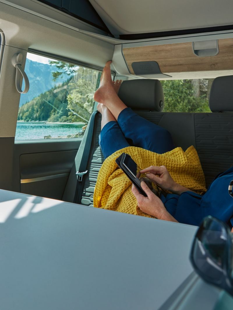 Woman reading on holiday in the back of a VW California 6.1 camper van in mountains
