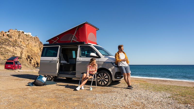 A couple relaxing inside a VW California parked next to a mountainside.