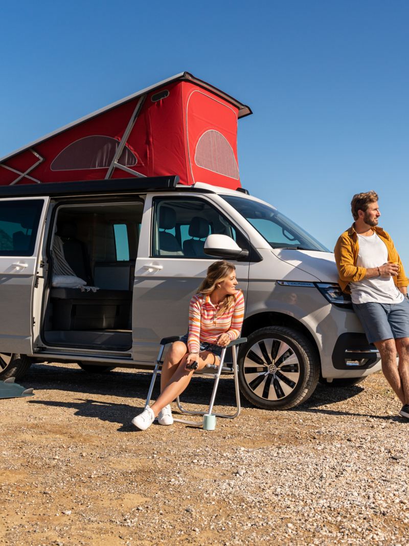 Vw Multivan parkt auf einem Strand am Meer mit ausgeklapptem Dachzelt und geöffneter Seitentür.