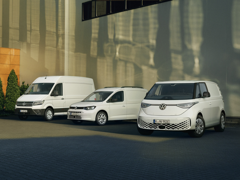 VW Crafter, VW Caddy und VW ID. Buzz parken in einer Reihe auf einem Parkplatz vor einem Gebäude.