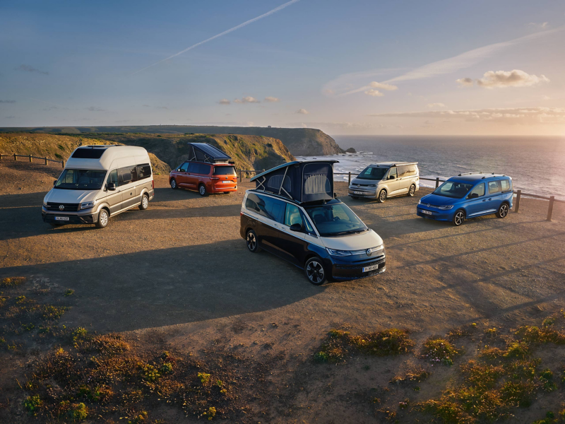 Drei VW California, ein Grand California und ein Caddy California parken nebeneinander an einer Steilküste.