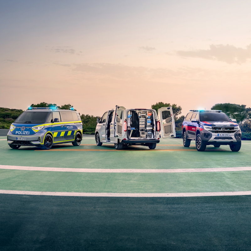 Drei umgebaute VW Nutzfahrzeuge stehen auf einem Platz.